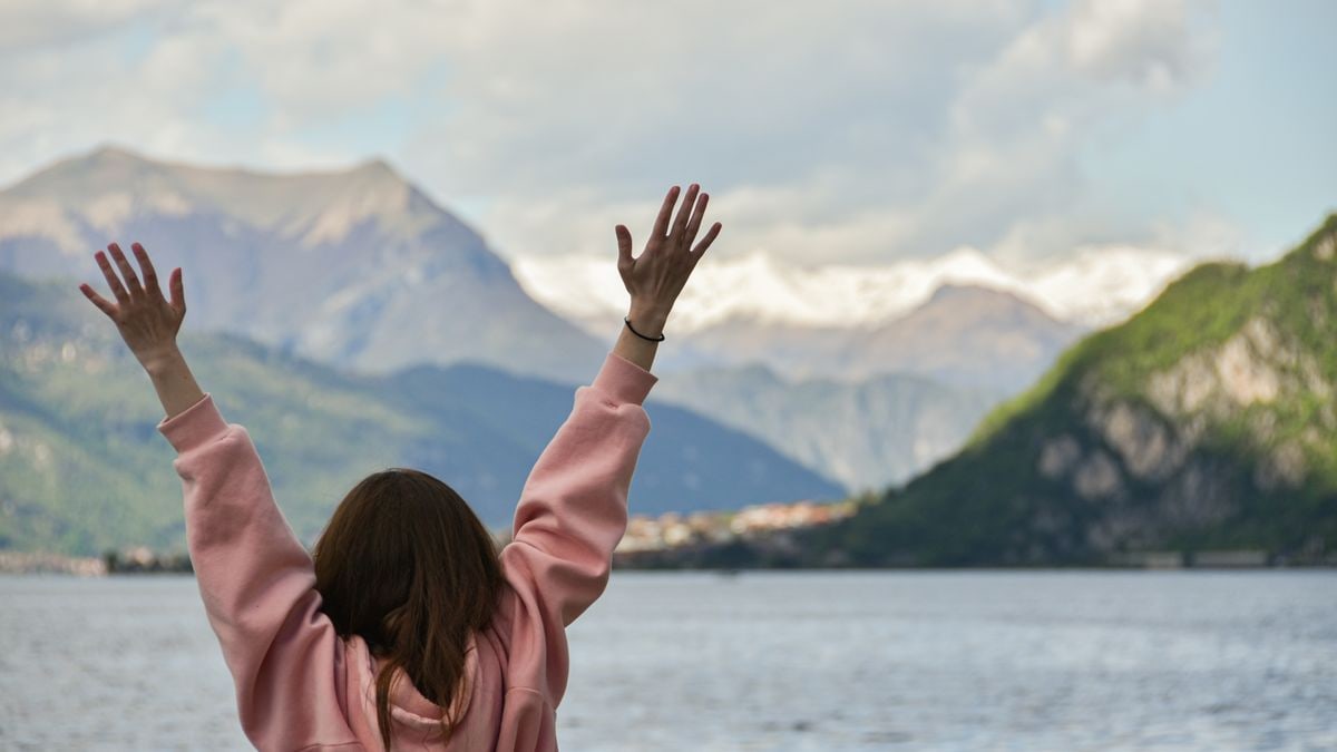 A woman with raised hands enjoying the scenic view of mountains and lake.