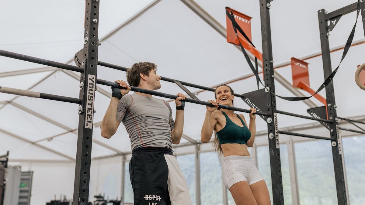 Man and woman exercising with pull-ups in an indoor gym, showcasing fitness and strength.